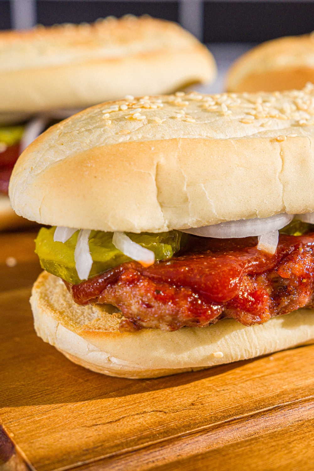 A wooden board with homemade McRib sandwiches on a hoagie roll with pickles, onions, and homemade BBQ sauce.