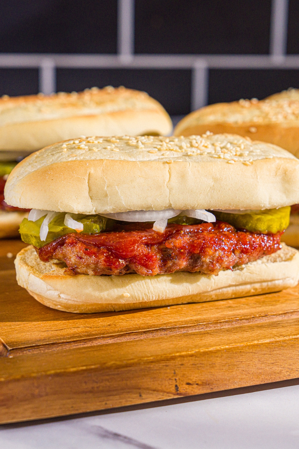 A wooden board with homemade McRib sandwiches on a hoagie roll with pickles, onions, and homemade BBQ sauce.