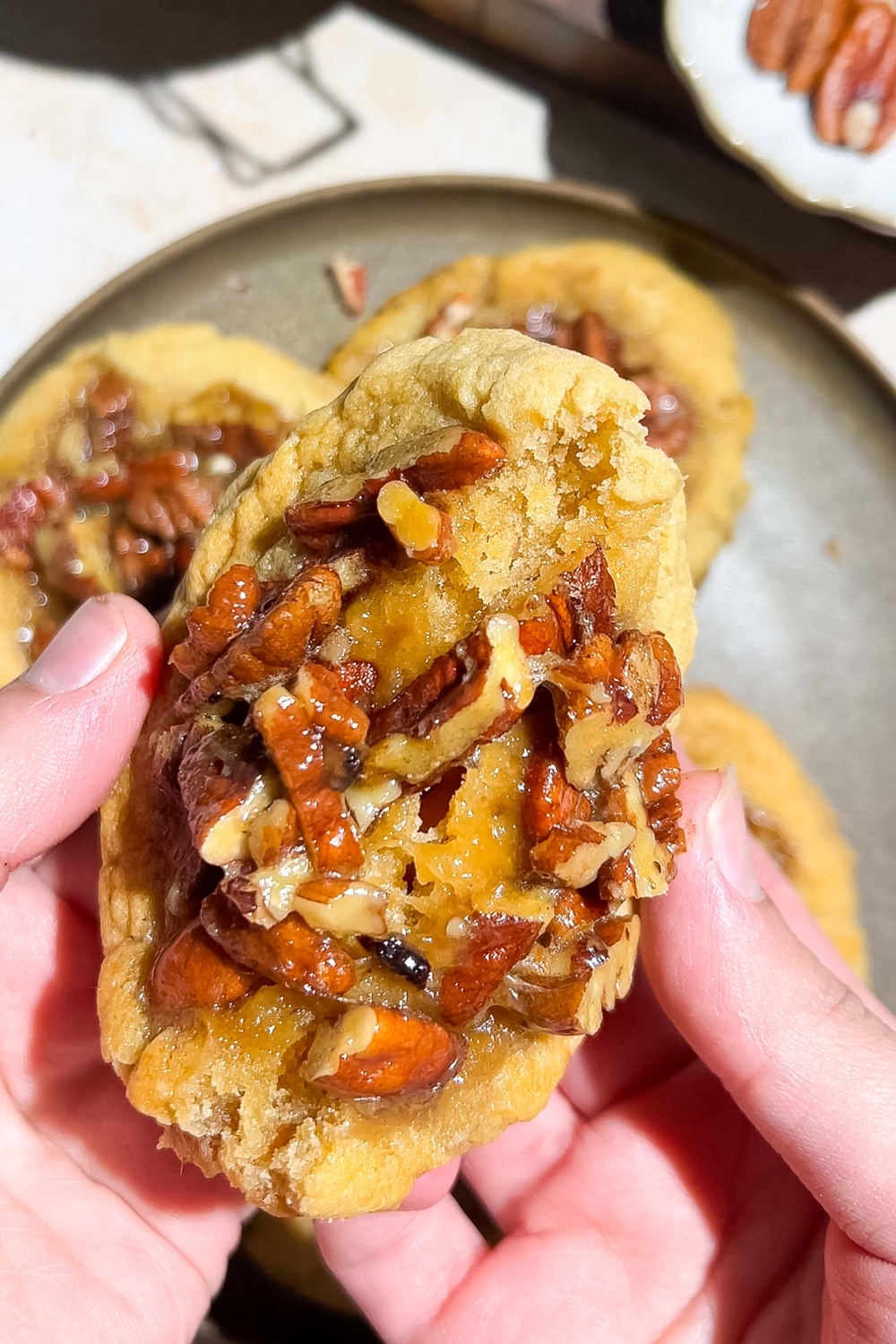 A close up of a hand folding apart a pecan pie cookie. There is a plate of cookies blurred in the background.