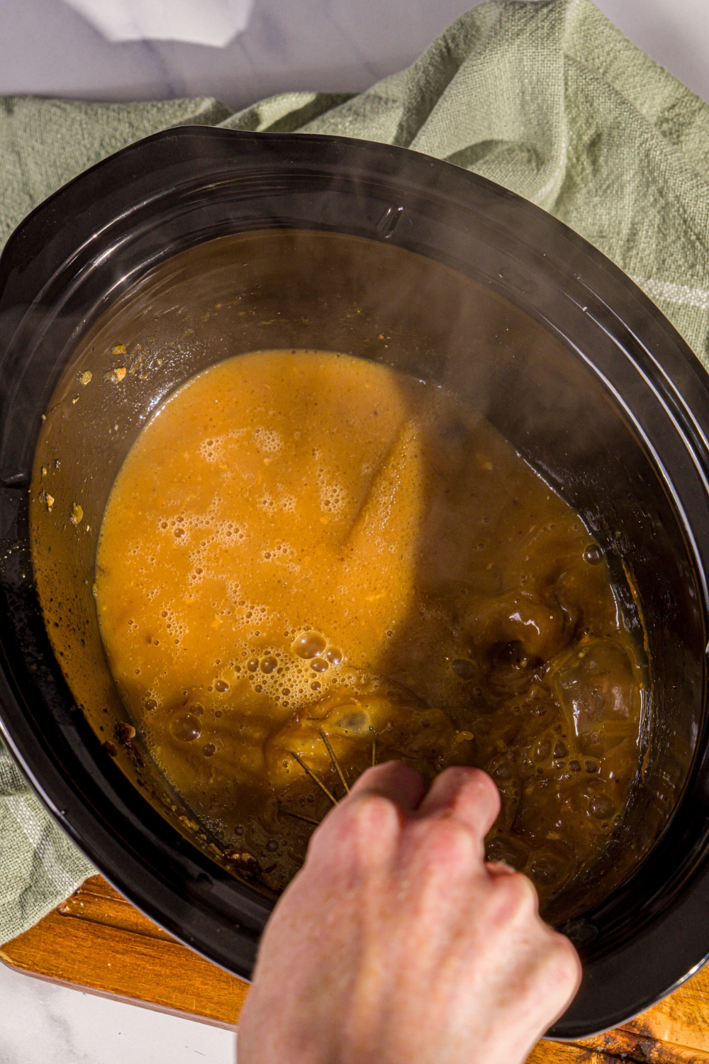 A crock pot with a whisk mixing ingredients to make gravy. The crock pot is on a wooden board.