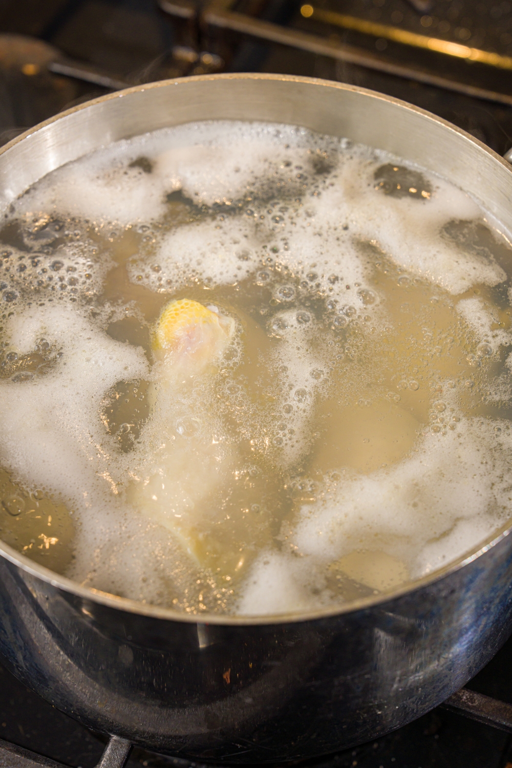 A stock pot with chicken legs in simmering water. The pot is cooking on the stove.