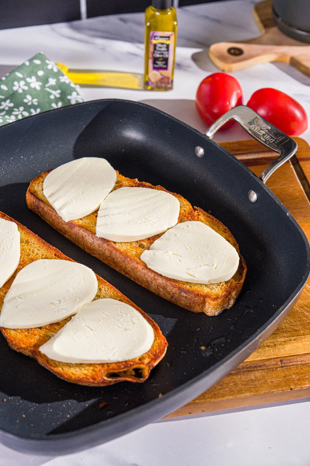 A skillet with two slices of toasted sourdough bread topped with sliced mozzarella. The skillet is on a wooden board.