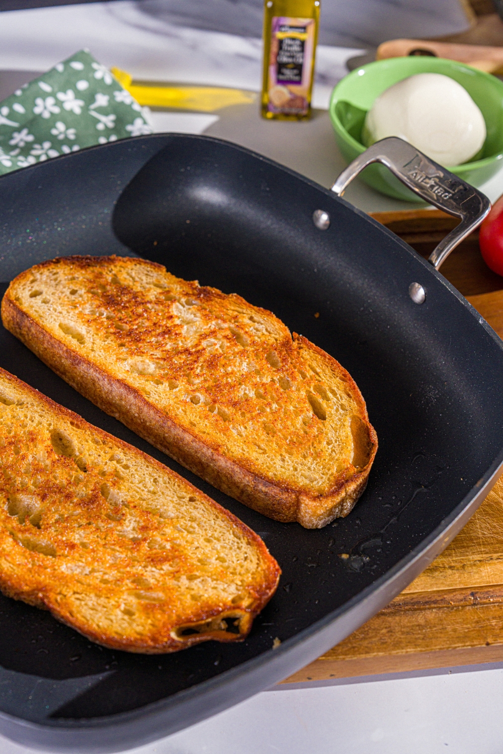 A skillet with two slices of toast sourdough bread. The skillet is on a wooden board.