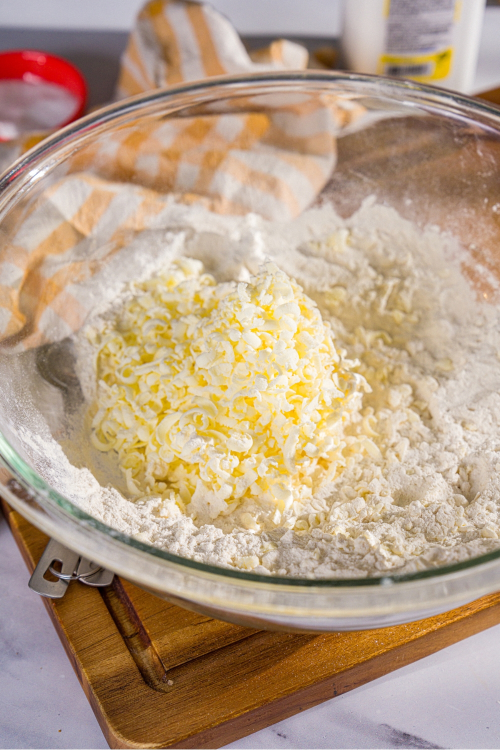 A large bowl with a dry ingredient mixture topped with grated butter. The bowl is on a wooden board.