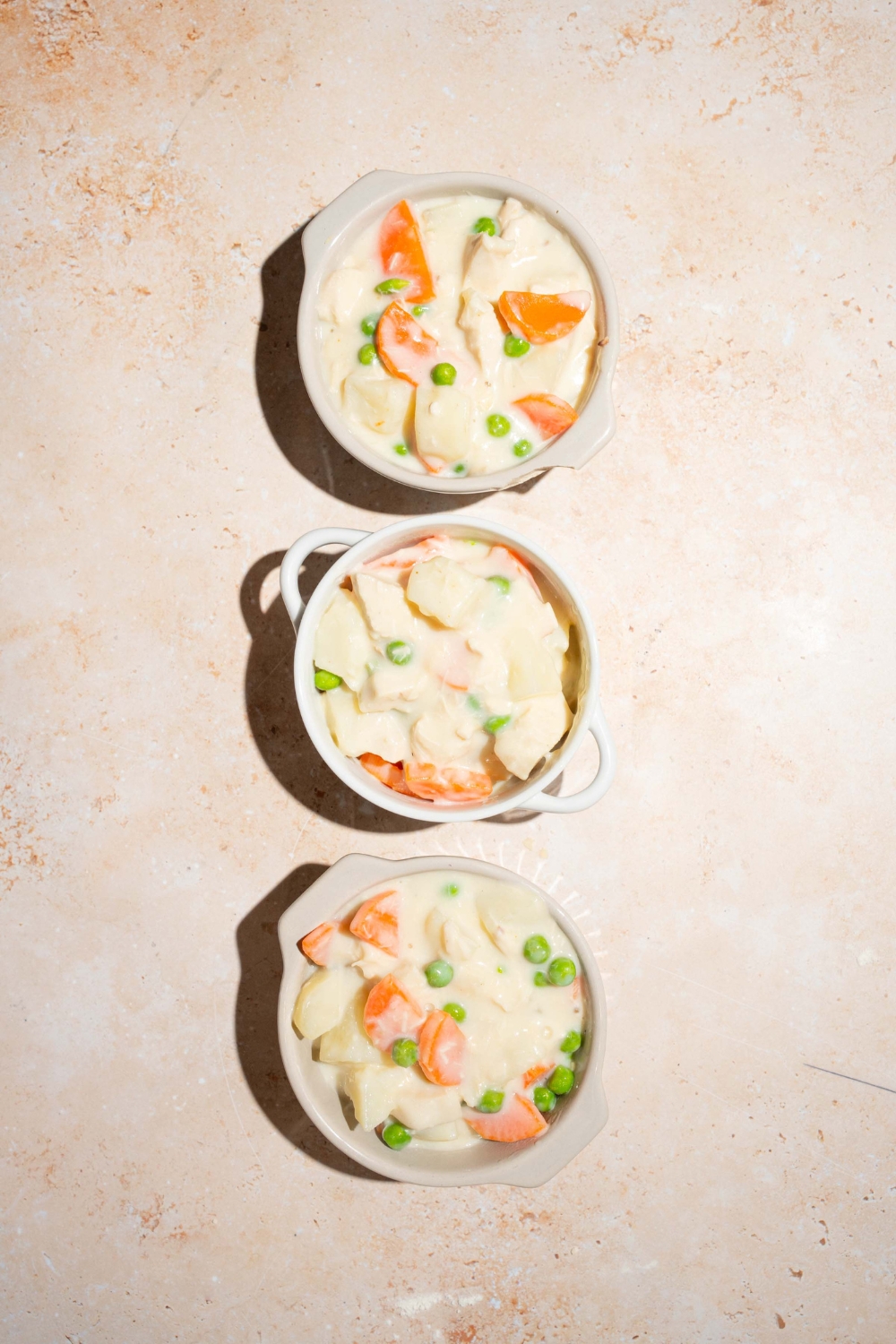 Three small pie tins with kfc pot pie filling. The tins are on a tan counter.