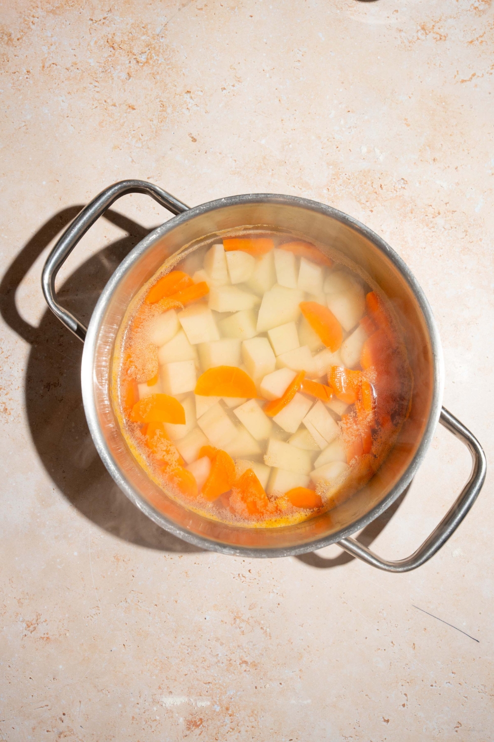 A large pot with potatoes and carrots cooking in water. The pot is on a tan counter.