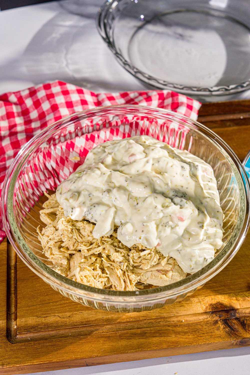 A large bowl with shredded chicken and broccoli cheddar soup. The bowl is on a wooden board with a red checkered napkin.