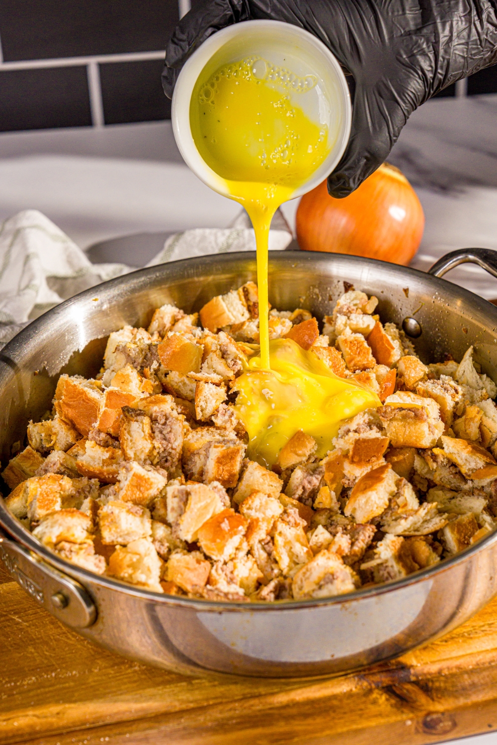 A large skillet with sliced White Castle sliders and sautéd vegetables with egg being added to mixture.