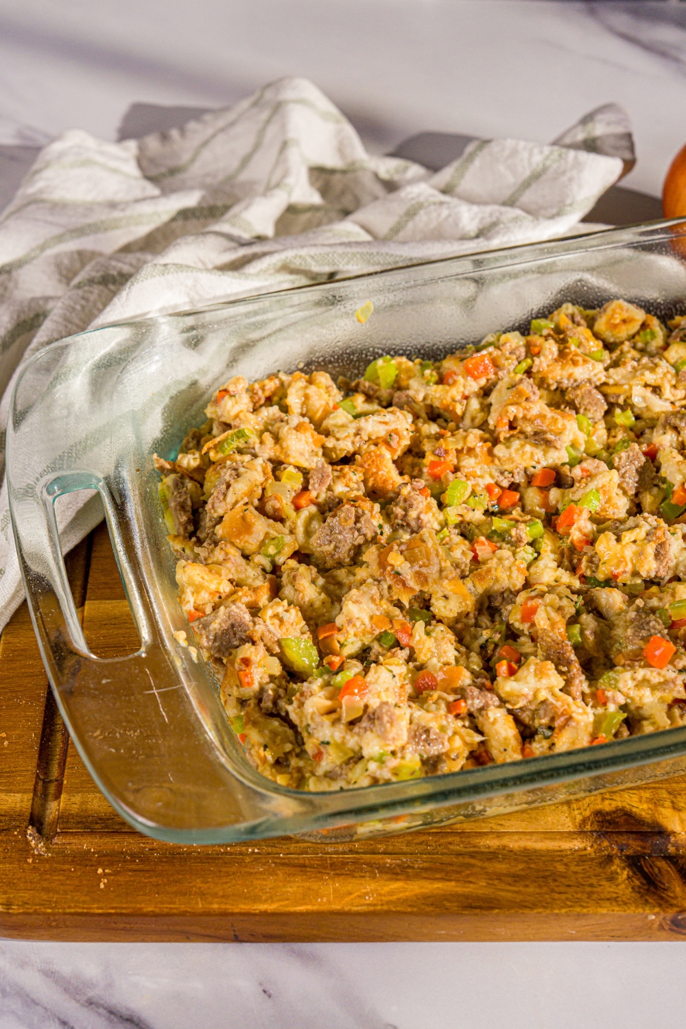 A baking dish with White Castle stuffing mixture including chopped White Castle sliders, sautéed vegetables, egg, and chicken stock. The dish is on a wooden board.