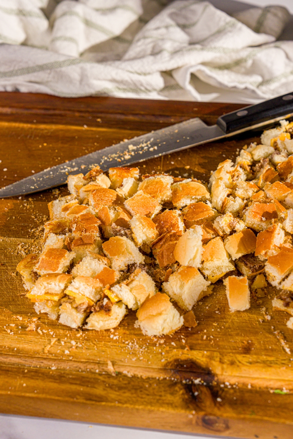 A wooden board with White Castle sliders cut up into bite sized pieces. There is a knife on the board.