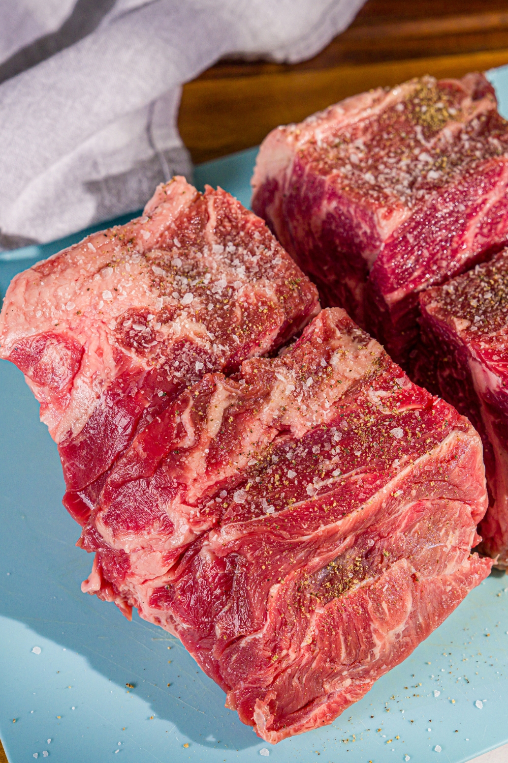 Chuck roast pieces seasoned with salt and pepper on a cutting board.