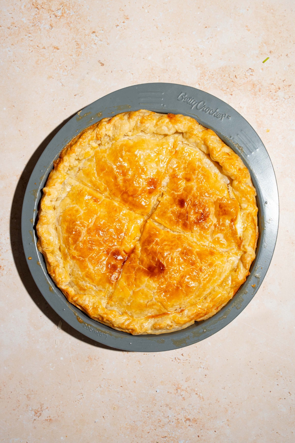 A whole baked meat pot pie on a gray platter. The platter is on a tan counter.