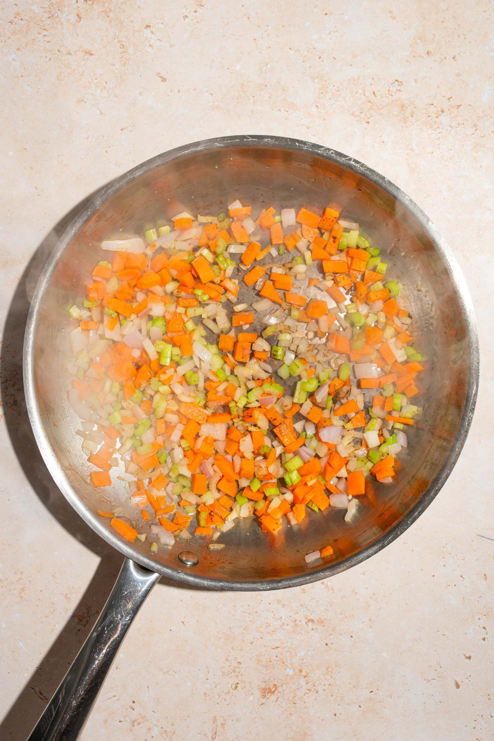 A skillet with sautéed carrots, celery, and onion. The skillet is on a tan counter.