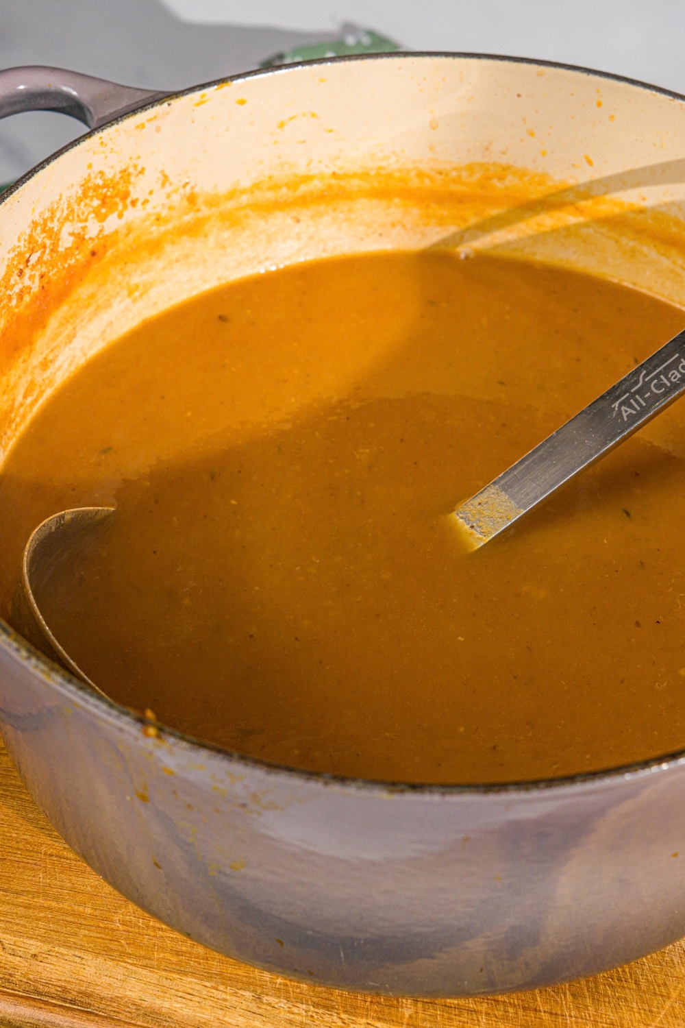 A large pot with a ladle stirring a shepherd's pie soup base. The pot is on a wooden board.