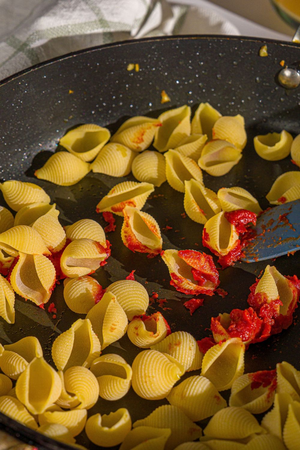 A skillet with shell pasta cooking with tomato paste.