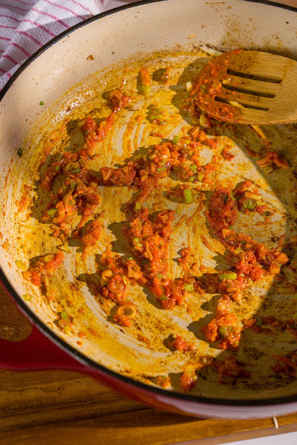 A cast iron skillet with sliced green onion, garlic, ginger paste, and red curry paste mixed together. The skillet is cooking on the stove.