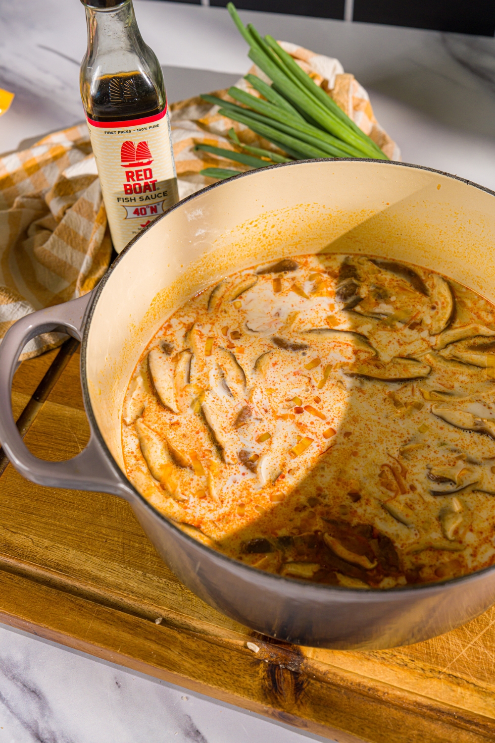 A dutch oven with a coconut red curry broth with mushrooms. The pot is on a wooden board.