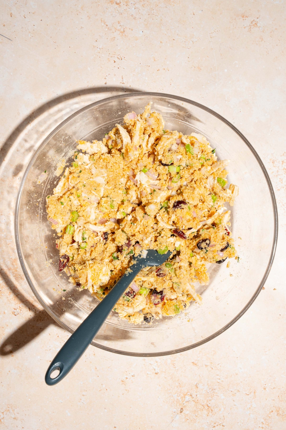 A large bowl with a rubber spoon mixing a cranberry turkey stuffing mixture. The bowl is on a tan counter.