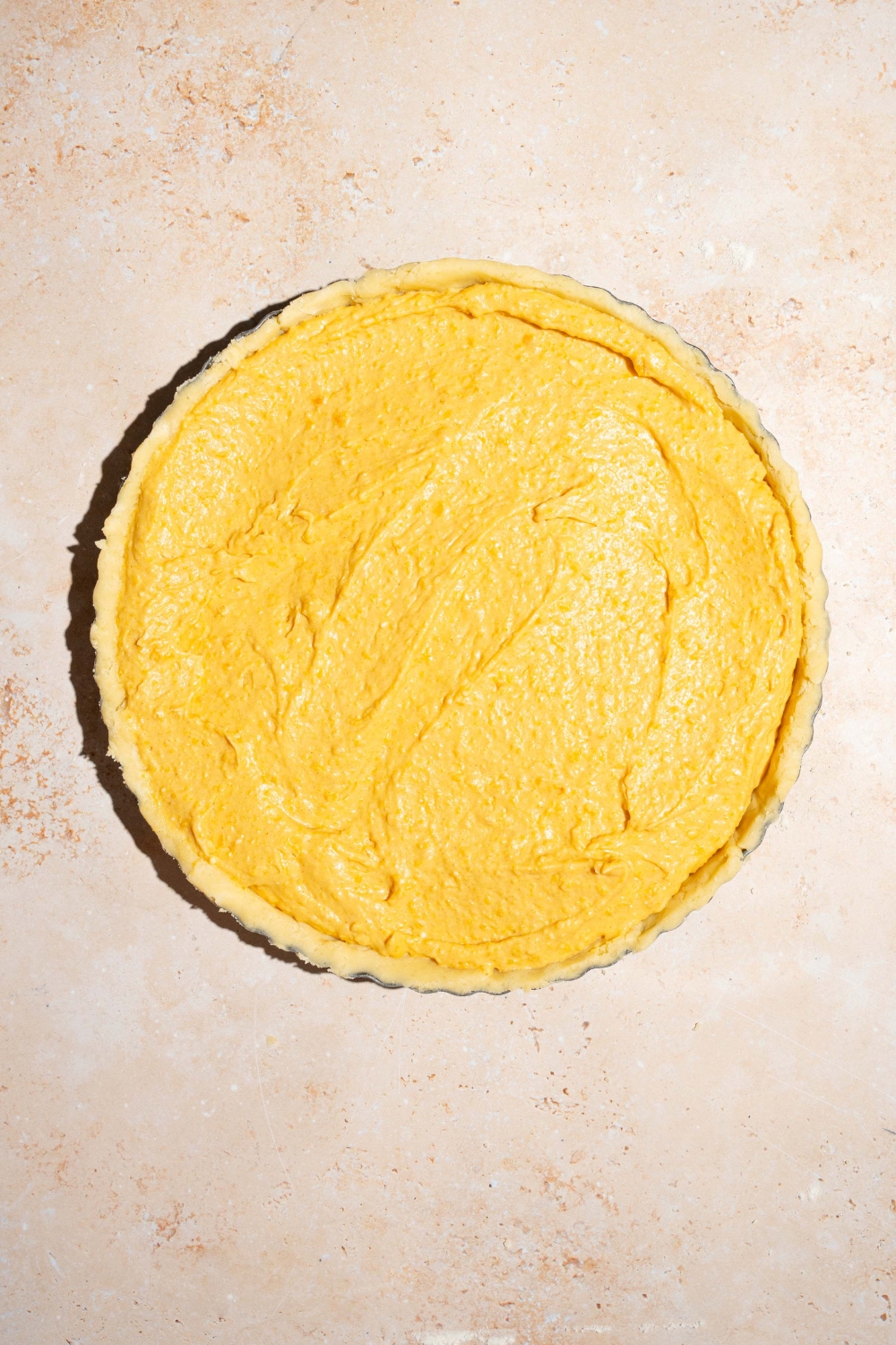 A whole unbaked cream cheese pumpkin pie. The pie is on a tan counter.