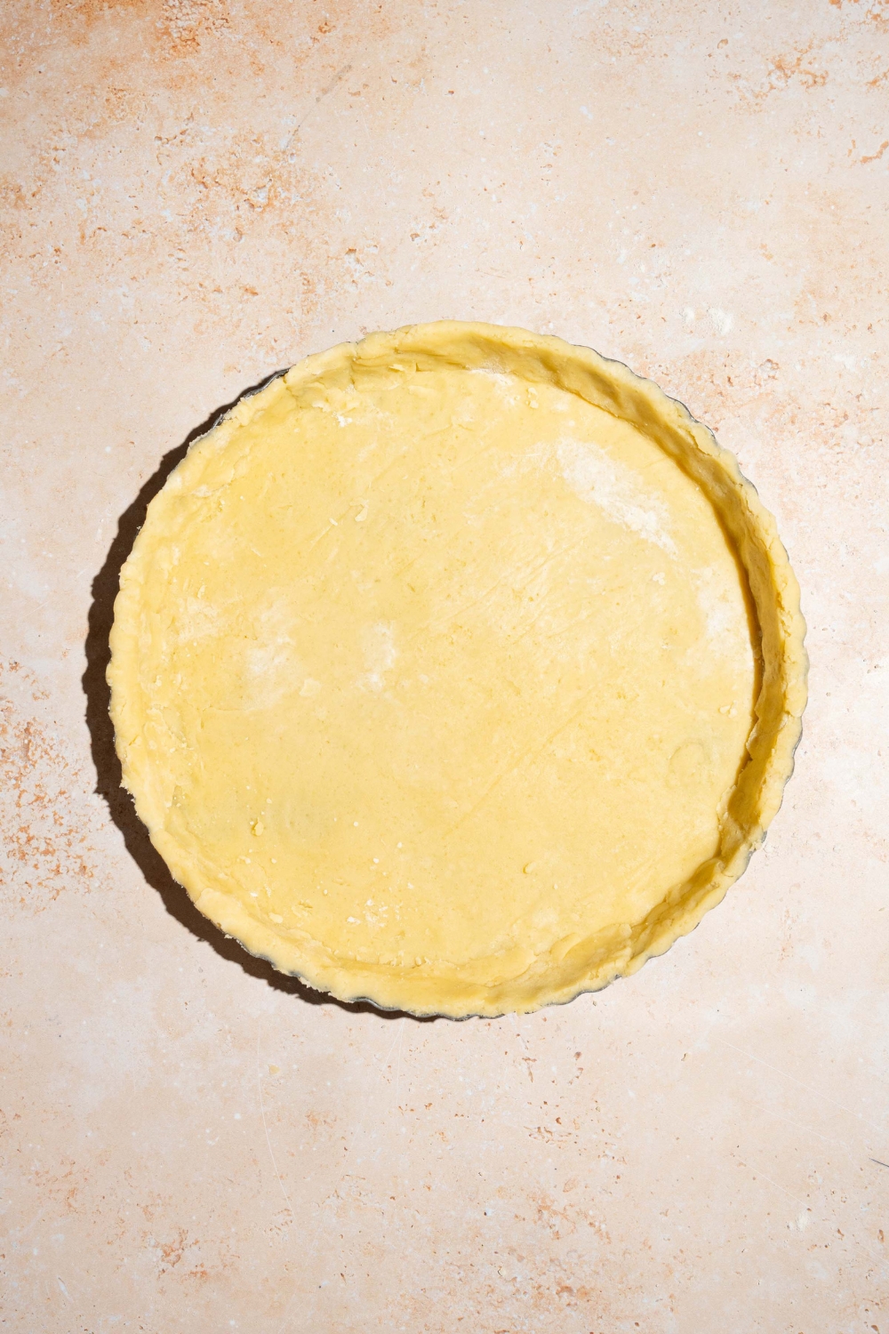 A pie plate covered with pie crust. The plate is on a tan counter.