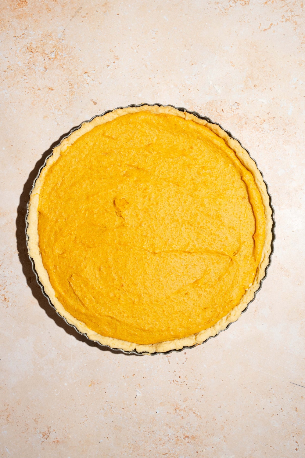 A whole unbaked cream cheese pumpkin pie. The pie is on a tan counter.