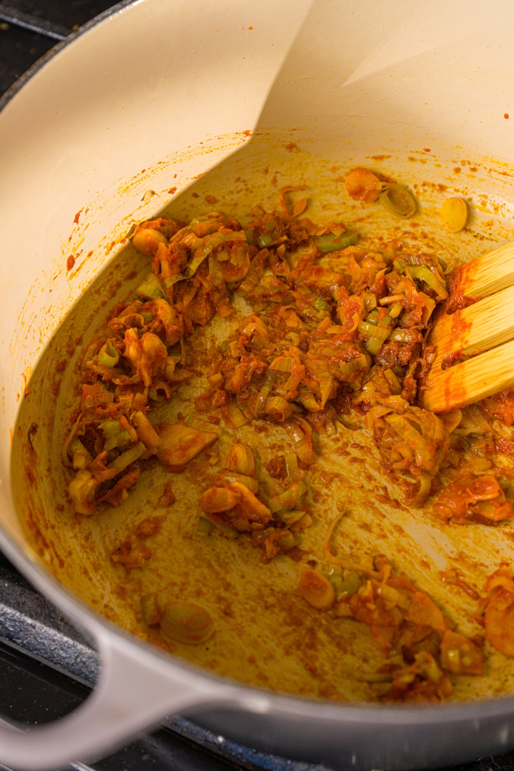 A dutch oven with leeks, garlic, ginger, and red curry. The pot is cooking on the stove.