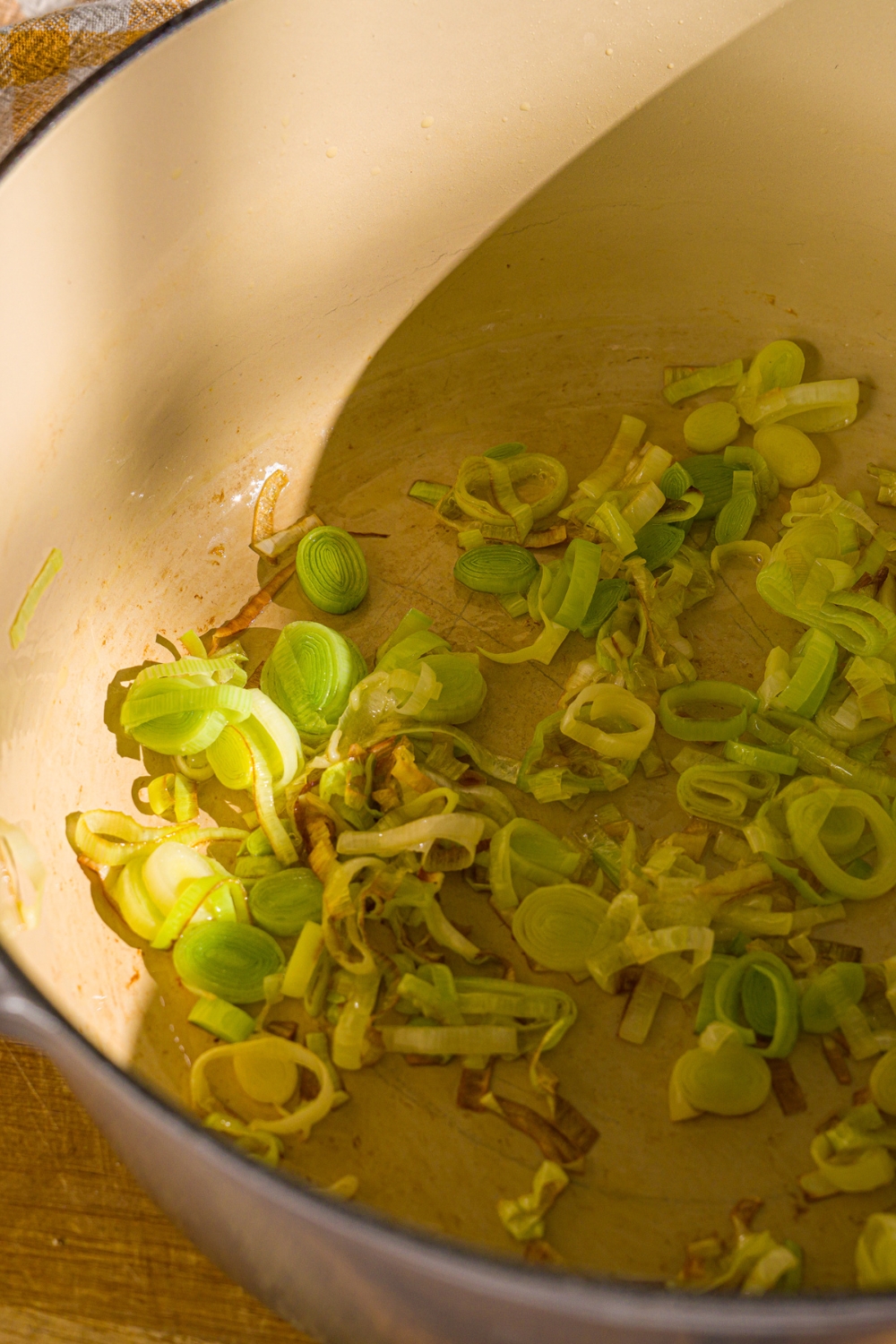 A dutch oven with sliced leeks cooking in oil.