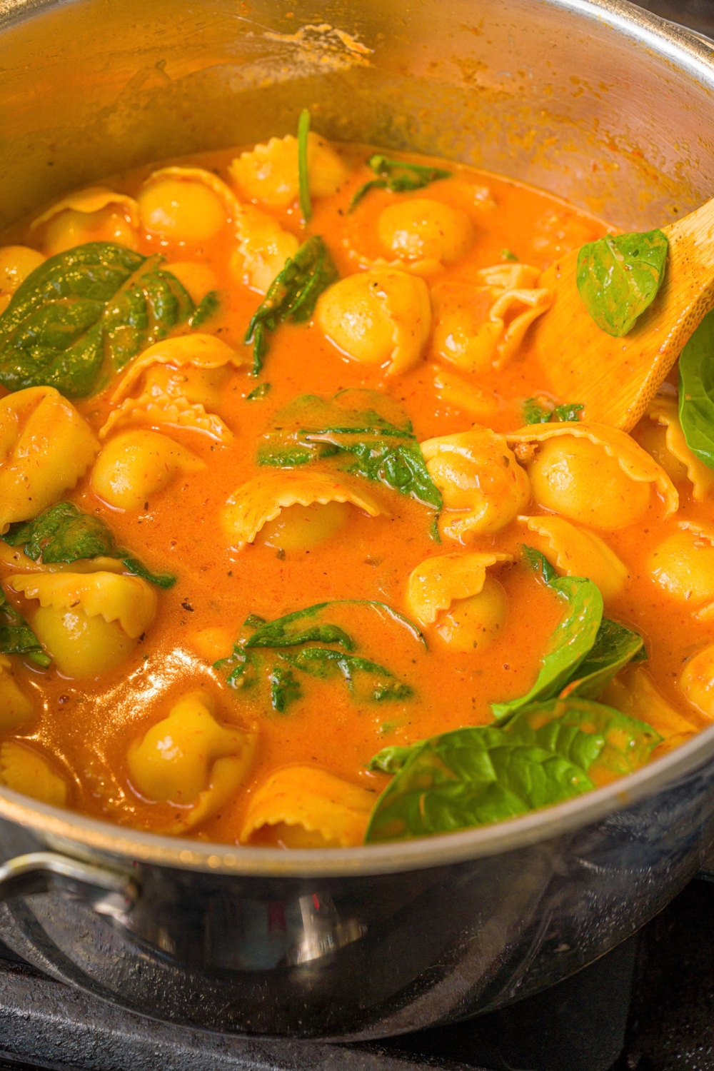 A pot with creamy tomato tortellini soup with spinach. The pot is cooking on the stove.