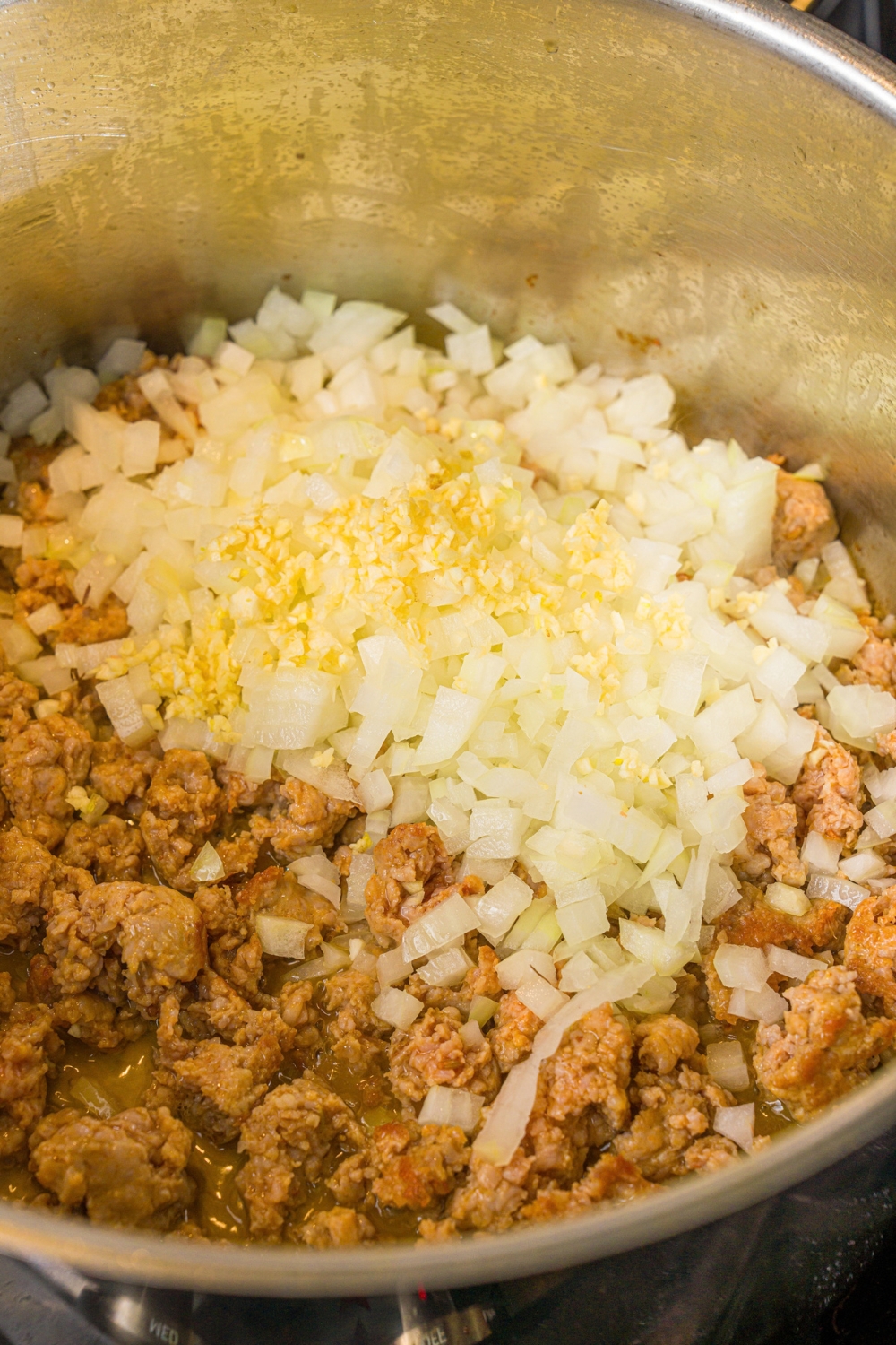 A large pot with browned ground sausage with white onion and garlic. The pot is cooking on the stove.
