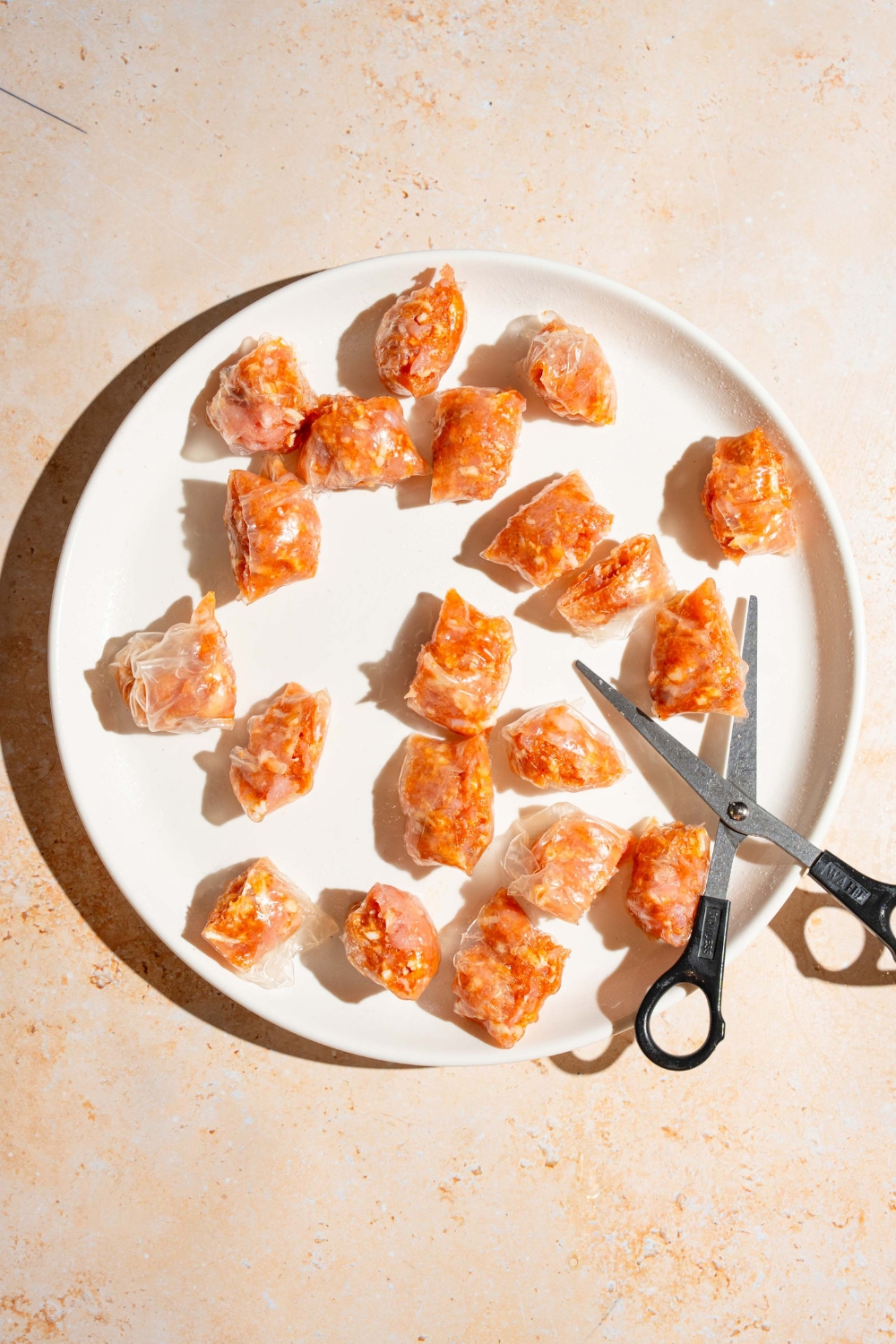 A white plate with rice paper wrapped chicken sliced into bite-size pieces with a pair of scissors. The plate is on a tan counter.