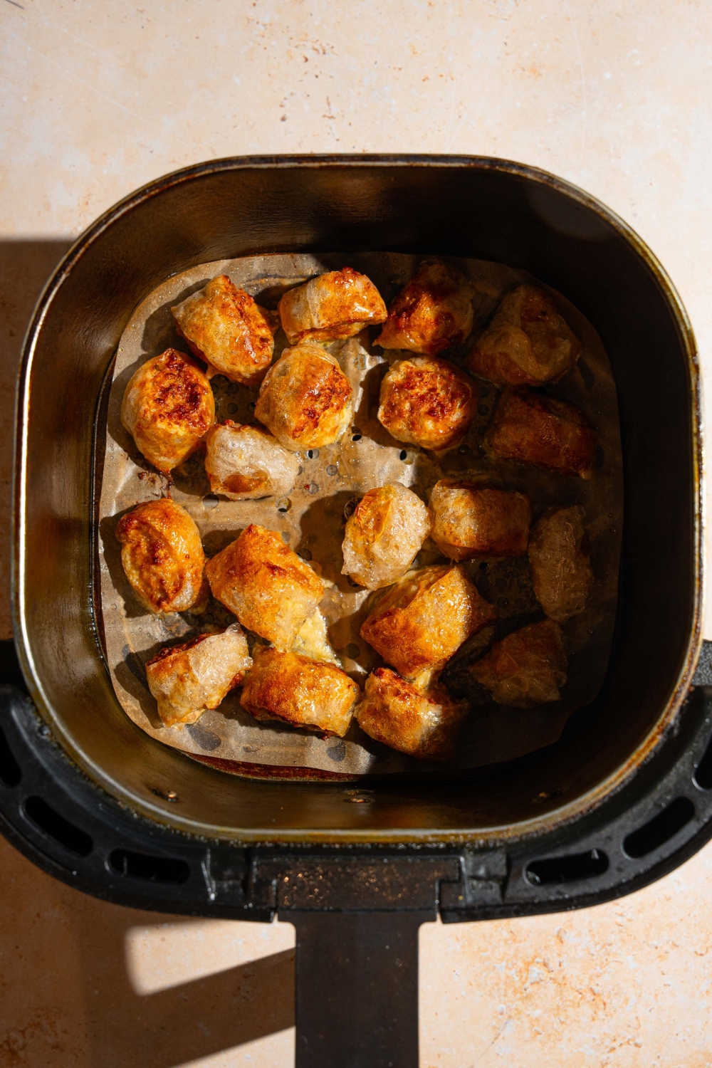 An air fryer basket with crispy rice paper chicken bites. The basket is on a tan counter.
