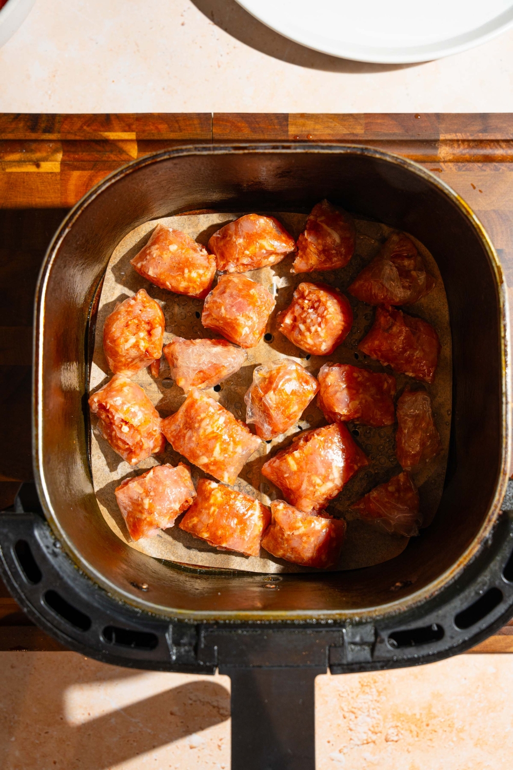 An air fryer basket with uncooked rice paper chicken bites. The basket is on a wooden board.