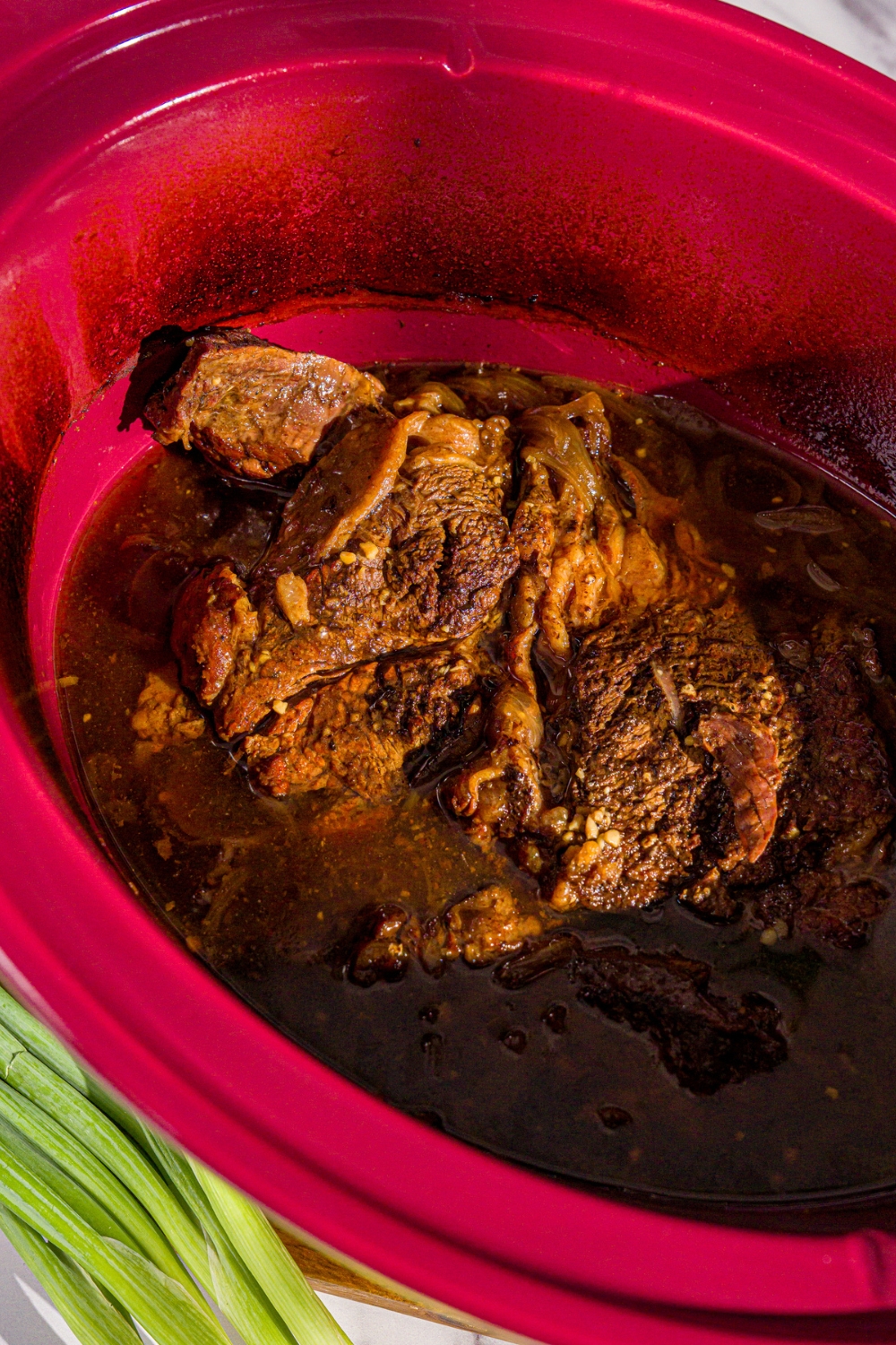 A crockpot with slow cooked chuck roast with a broth mixture.
