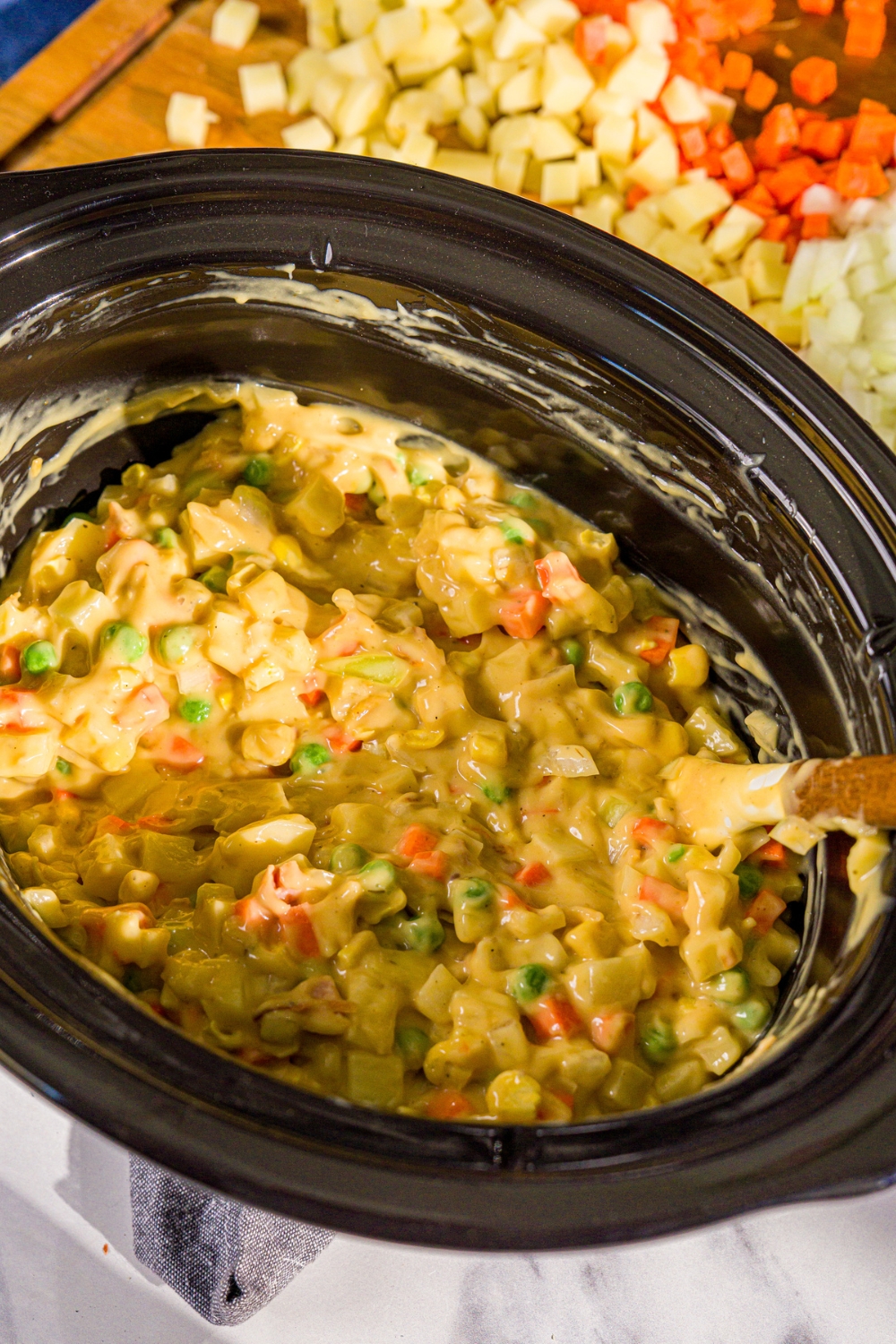 A crockpot with a vegetable and soup pot pie mixture with a rubber spoon in the pot. The pot is on a marble counter.