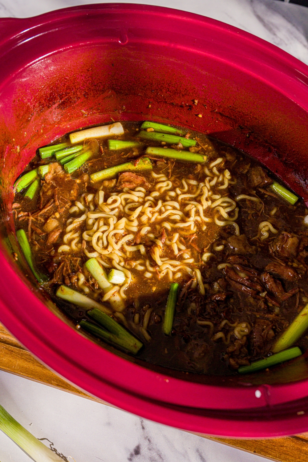 A crock pot with Mongolian beef sauce with noodles and green onions.