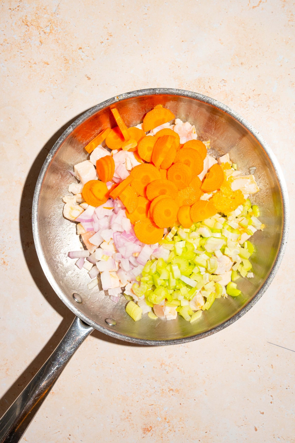 A skillet with sliced carrots, celery, and onion. The skillet is on a tan counter.