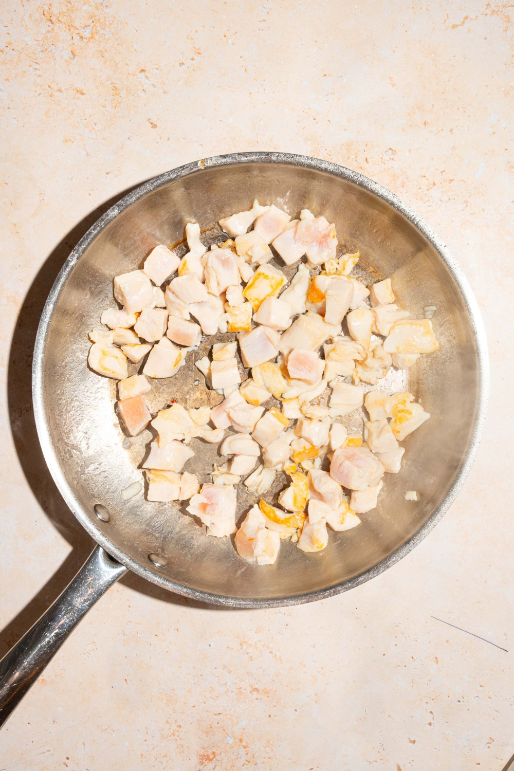 A skillet with browned chicken cubes. The skillet is on a tan counter.