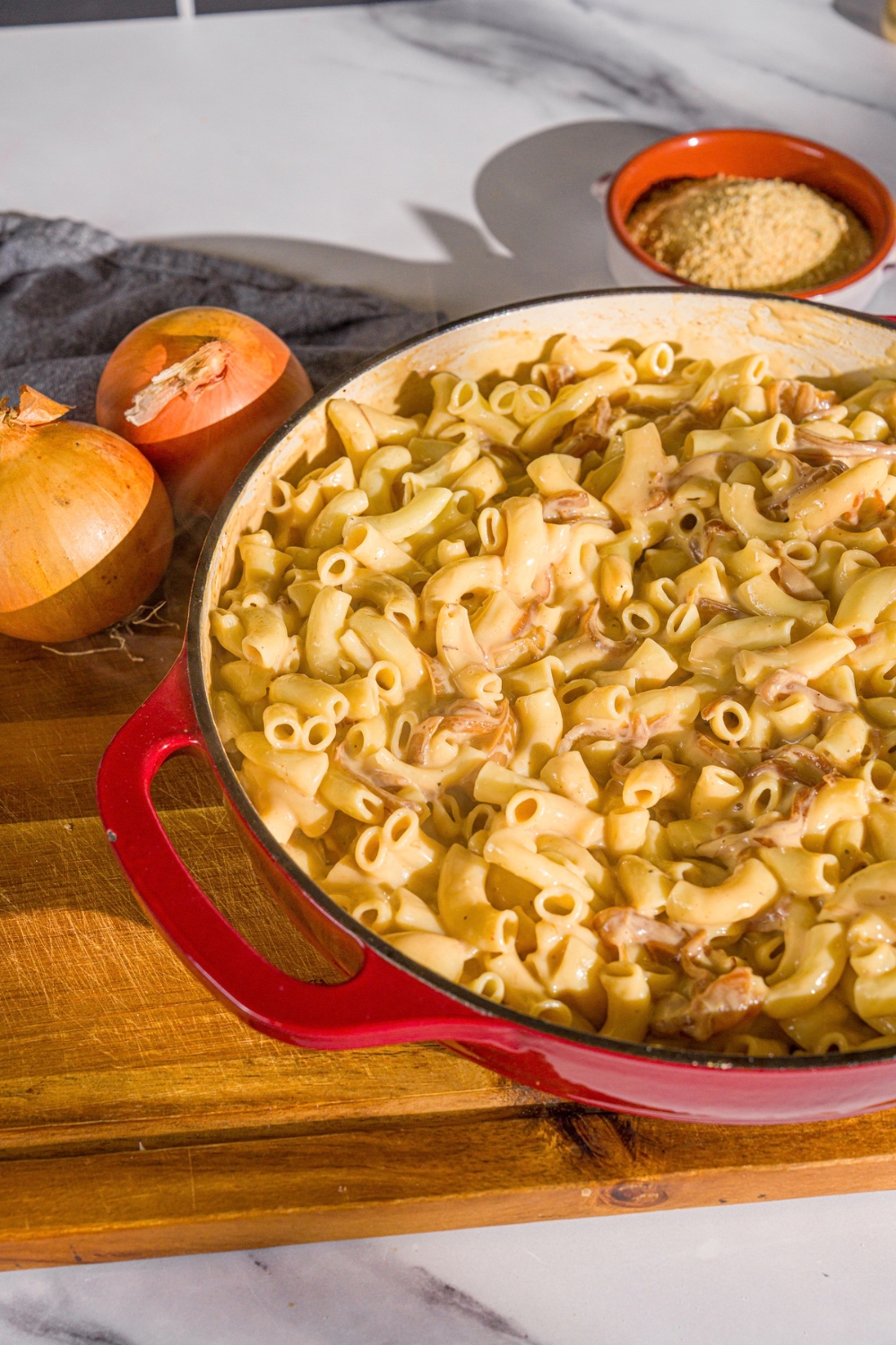 A cast iron skillet with macaroni tossed in a French onion cheese sauce. The skillet is on a wooden board with onions.