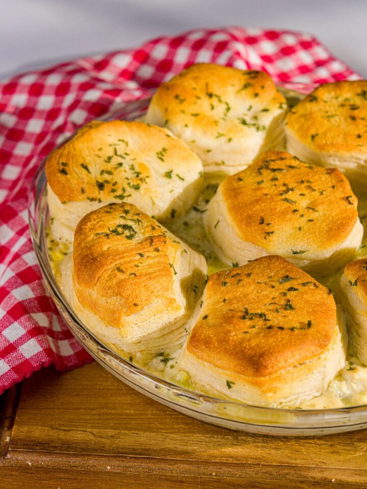 A round baking dish with baked Trader Joe's chicken pot pie with a biscuit topping. The dish is on a wooden board with a red checkered napkin.