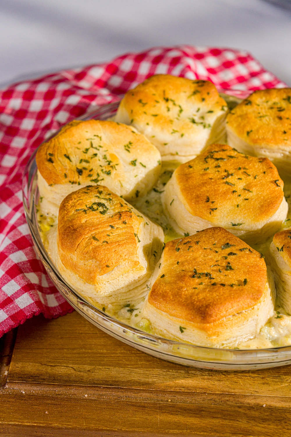 A round baking dish with baked Trader Joe's chicken pot pie with a biscuit topping. The dish is on a wooden board with a red checkered napkin.