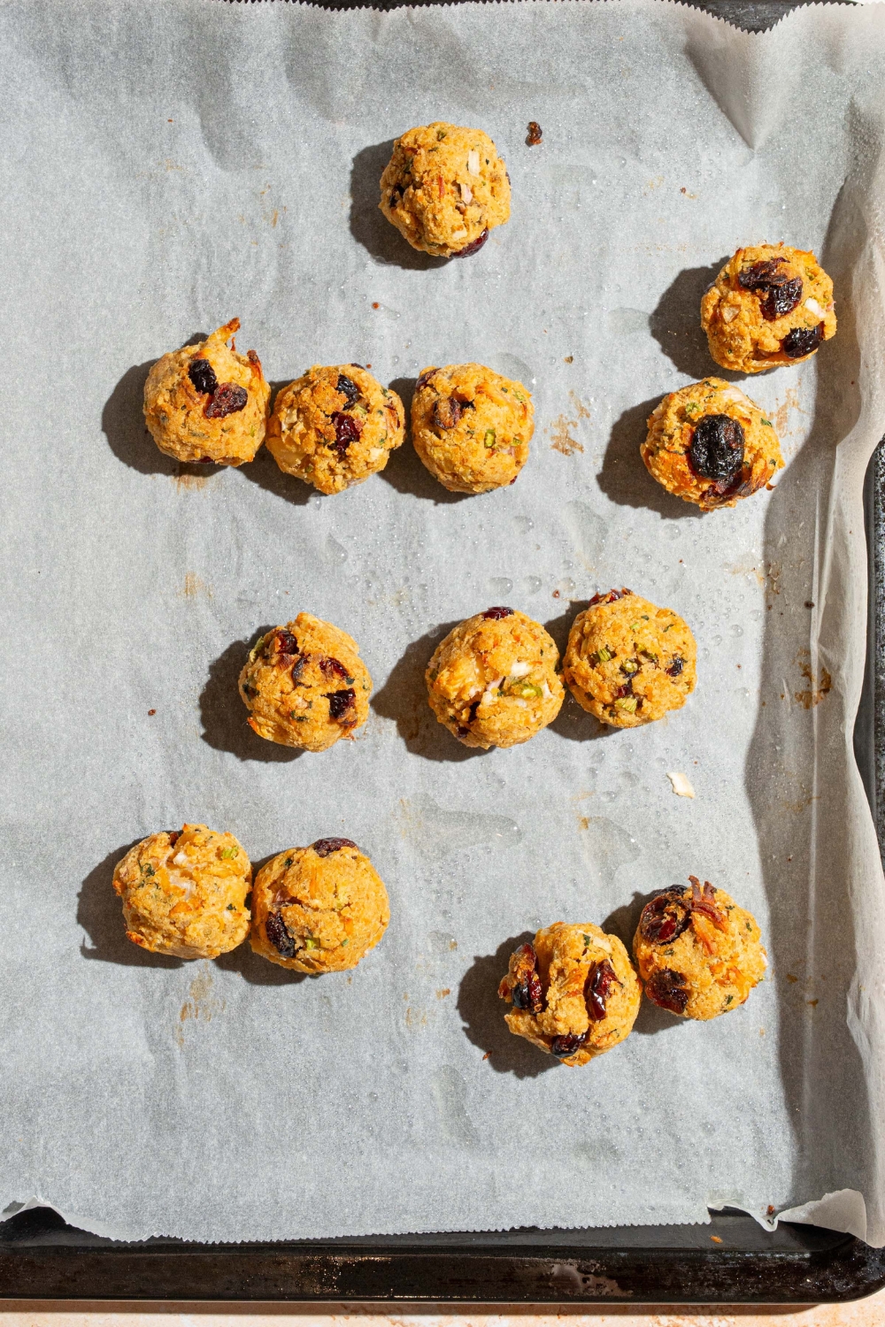 A baking sheet lined with parchment paper with baked cranberry turkey stuffing balls.