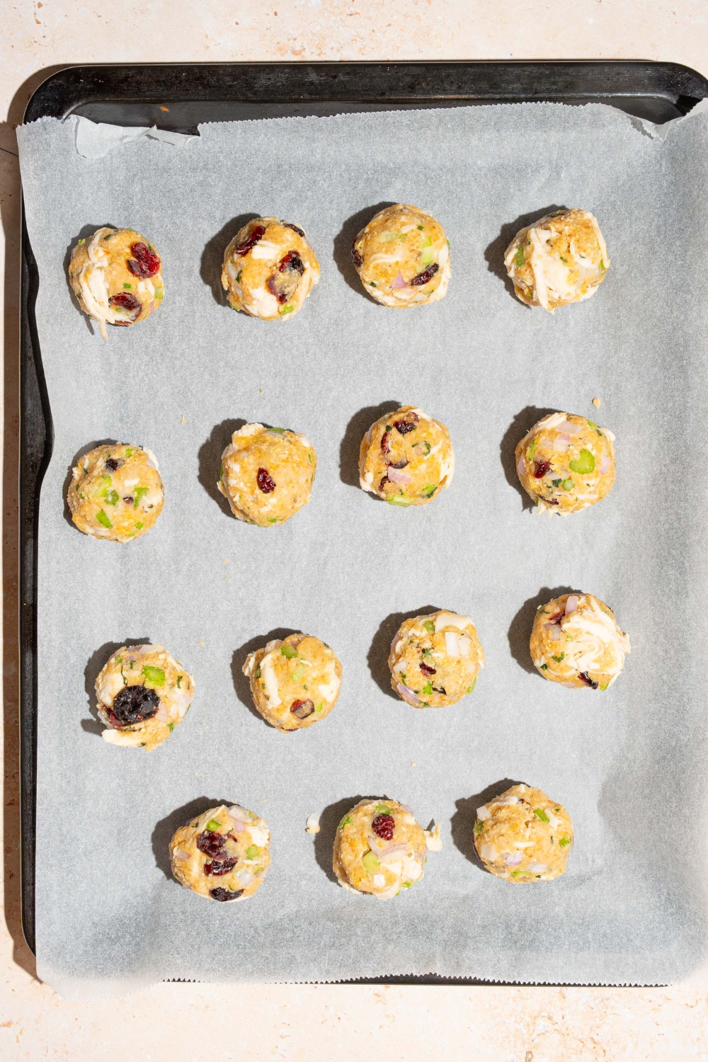 A baking sheet lined with parchment paper with unbaked cranberry turkey stuffing balls.