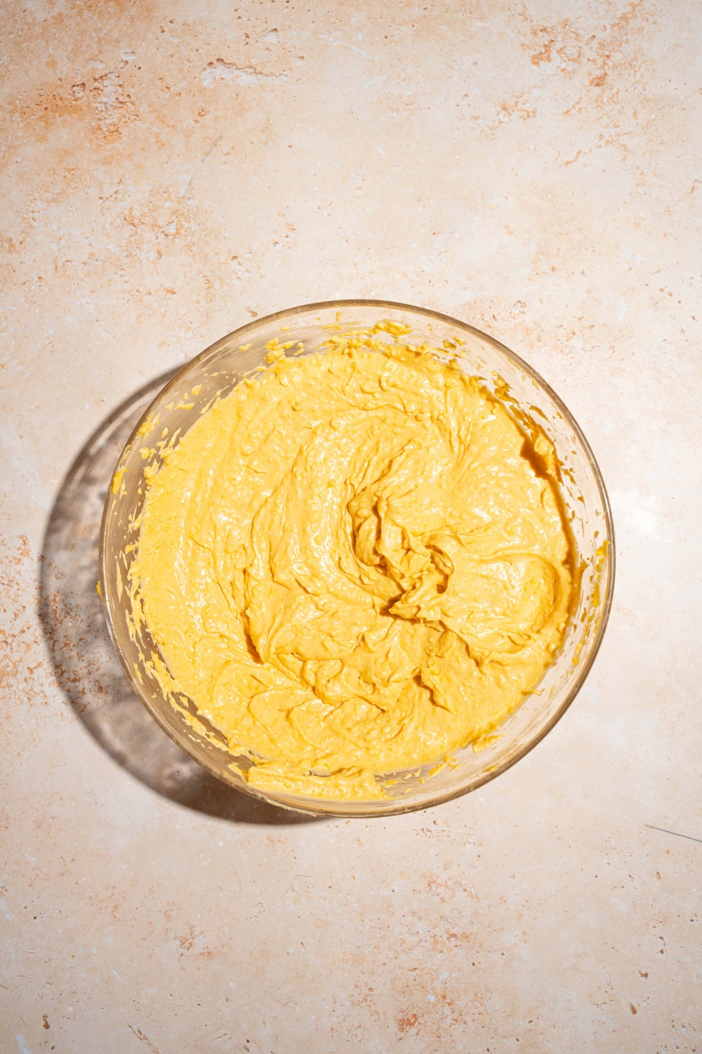 A large bowl with whisked cream cheese pumpkin pie filling. The bowl is on a tan counter.