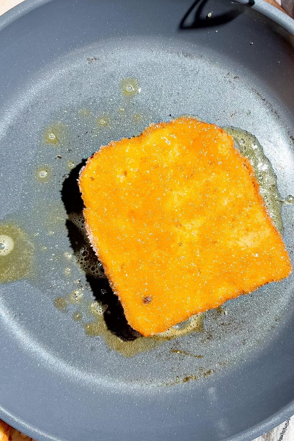 A slice of brioche bread soaked in custard and coated in sugar cooking on a stove.