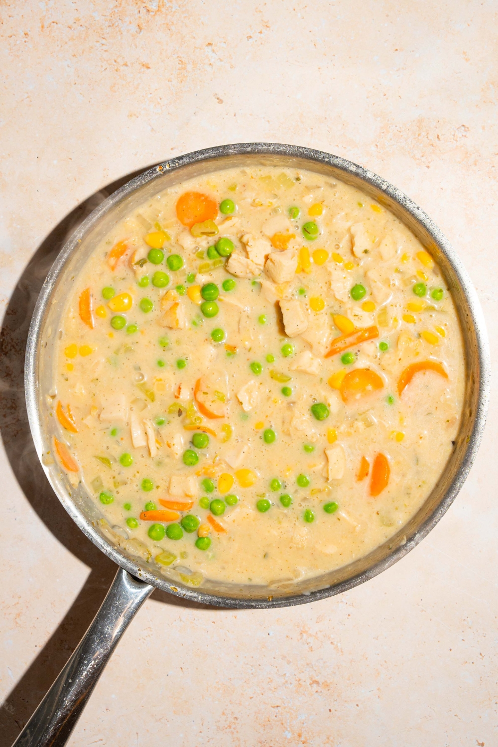 A skillet with crustless chicken pot pie mixture with chicken, carrots, celery, peas, and carrots in a milk and broth mixture.