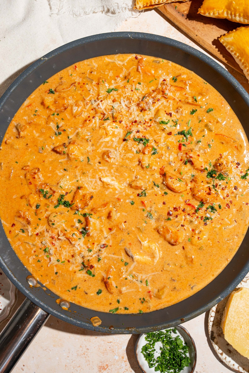 A skillet with seafood pot pie filling garnished with fresh parsley. The skillet is on a tan counter with a small bowl of garnishes.