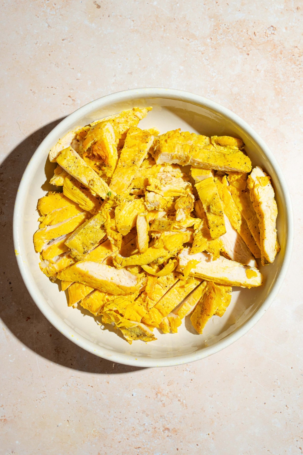 A large bowl with sliced cooked chicken. The bowl is on a tan counter.