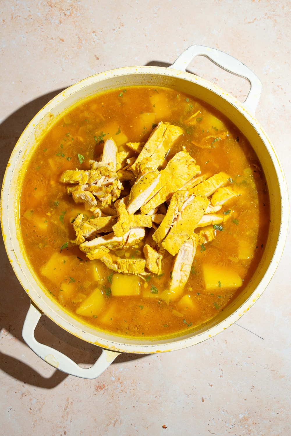 A large pot of garlic chicken soup base topped with sliced chicken. The pot is on a tan counter.