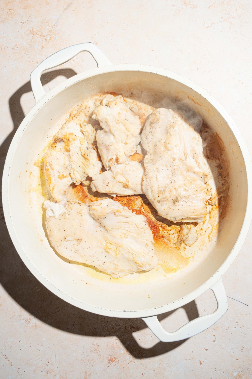 A large pot with seared chicken breasts. The pot is on a tan counter.