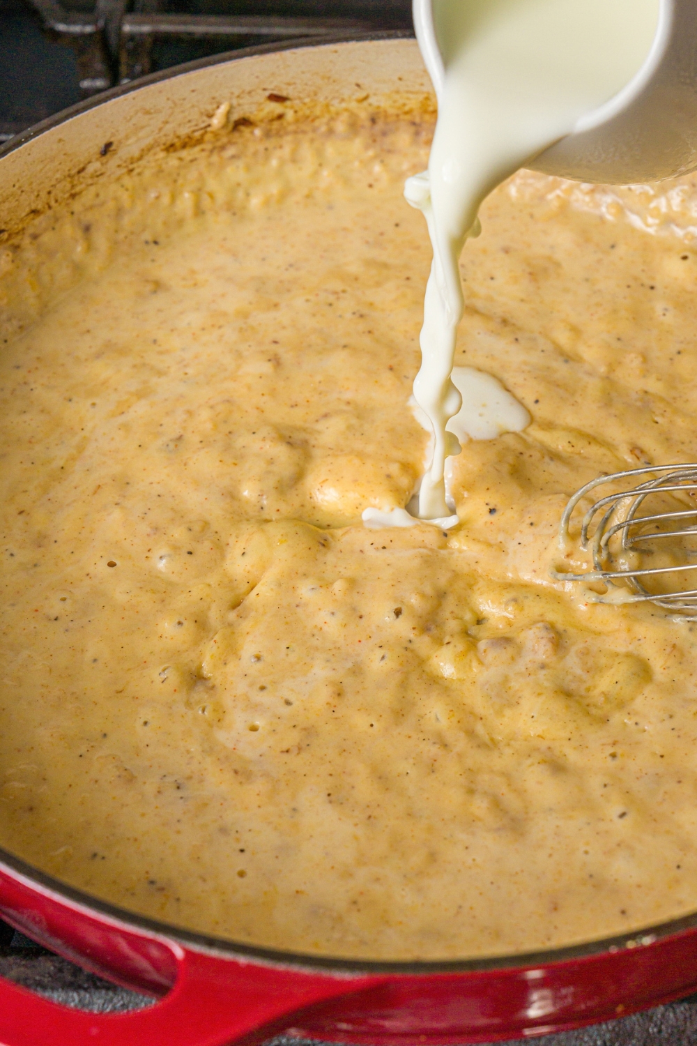 A skillet with milk being added to a roux to make French onion mac and cheese.The skillet is cooking on a stove.